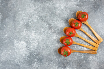 Wooden spoons of red fresh tomatoes on marble background