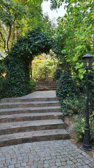Path through arched gateway to English walled garden. Stone paved stairs in park with retro streetlight lantern