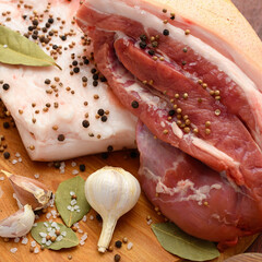 raw pork meat and lard with salt, spices and garlic on a cutting board, dark wooden background