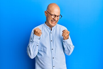 Middle age bald man wearing casual clothes and glasses excited for success with arms raised and eyes closed celebrating victory smiling. winner concept.