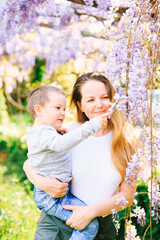 Mother is holding her 6-year old in her arms and showing him wysteria tree