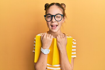 Beautiful brunette little girl wearing glasses and holding book winking looking at the camera with...