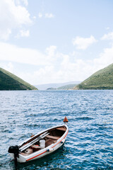 A white fishing boat sways on the water against the backdrop of the picturesque countryside of Perast.