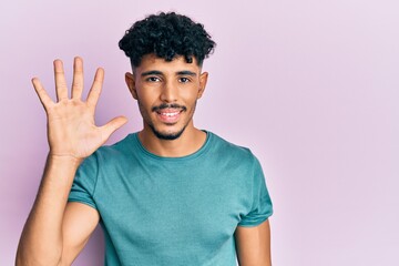 Young arab handsome man wearing casual clothes showing and pointing up with fingers number five while smiling confident and happy.
