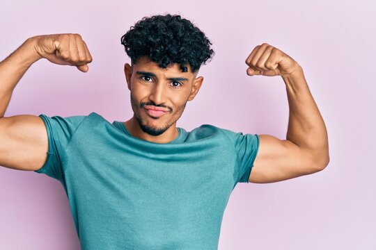 Young arab handsome man wearing casual clothes showing arms muscles smiling proud. fitness concept.