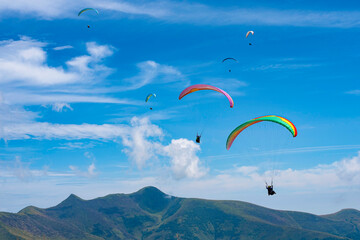 Young people fly paragliders in summer in the Carpathian mountains against a beautiful blue sky, people feel free and enjoy the view from above on landscapes