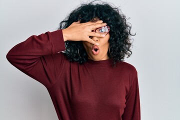 Fototapeta na wymiar Young hispanic woman wearing casual clothes and glasses peeking in shock covering face and eyes with hand, looking through fingers afraid