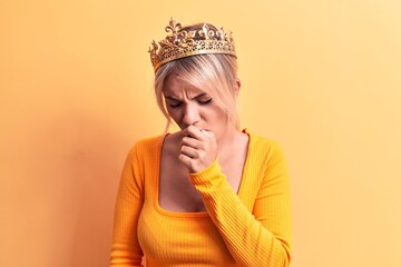 Young beautiful blonde woman wearing golden princess crown over isolated yellow background feeling unwell and coughing as symptom for cold or bronchitis. Health care concept.