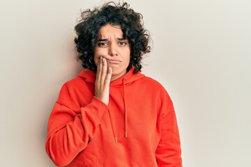 Young hispanic woman with curly hair wearing casual sweatshirt touching mouth with hand with painful expression because of toothache or dental illness on teeth. dentist