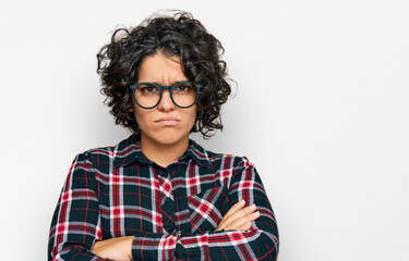 Young hispanic woman with curly hair wearing casual clothes and glasses skeptic and nervous, disapproving expression on face with crossed arms. negative person.