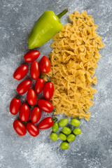 Uncooked farfalle and vegetables on marble background