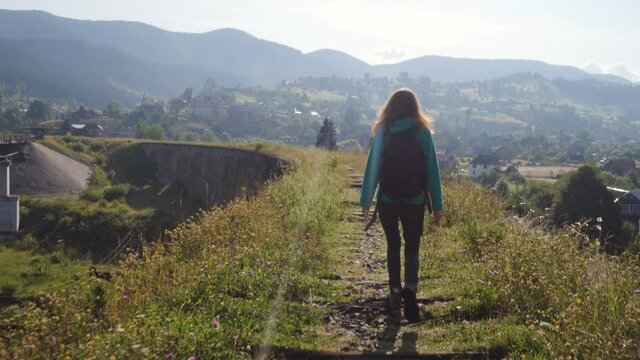 hiker girl crossing the old stone bridge over the mountain river at the bright summer day
