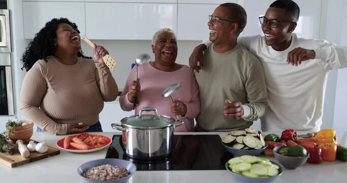 Happy black family having fun cooking and dancing together inside kitchen at home 