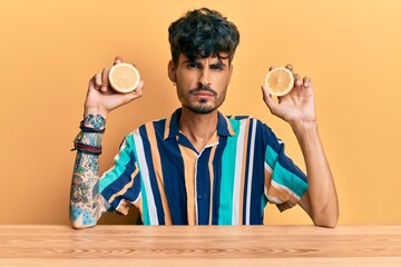 Young hispanic man sitting on the table holding lemon skeptic and nervous, frowning upset because of problem. negative person.
