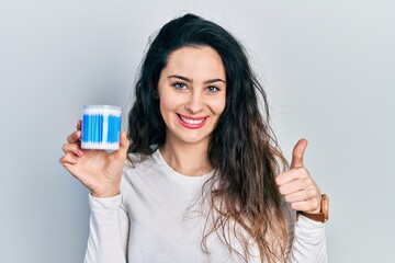 Young hispanic woman holding earwax cotton remover smiling happy and positive, thumb up doing excellent and approval sign