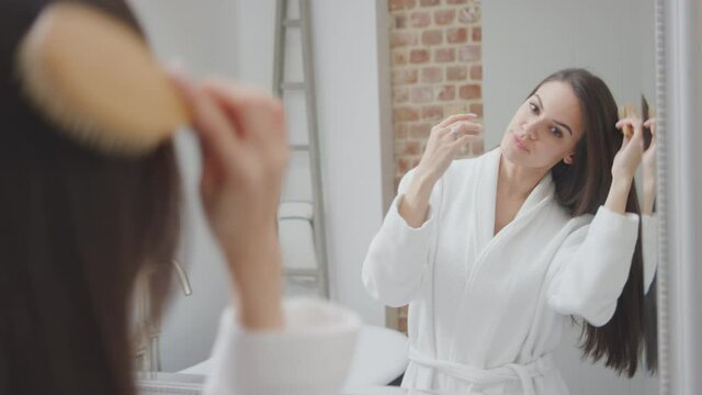 Reflection of couple wearing bathrobe and pyjamas getting ready brushing hair and teeth in bathroom mirror at home - shot in slow motion