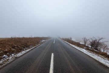 Fototapeta na wymiar Asphalt road leading to the top of the hill at wintertime in dense fog with low visibility.