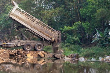 The truck was pouring rocks to fill the river.