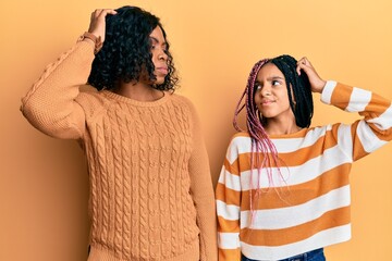 Beautiful african american mother and daughter wearing wool winter sweater confuse and wondering...