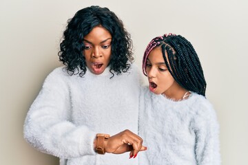 Beautiful african american mother and daughter wearing casual winter sweater looking at the watch...