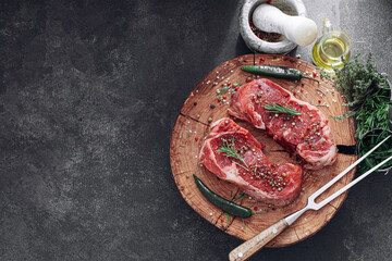 fresh raw striploin steak on a wooden board on a wooden background with salt and pepper in a rustic...