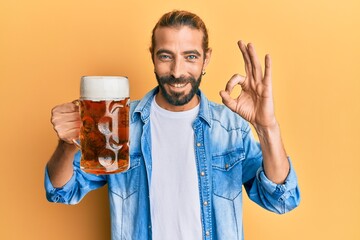 Attractive man with long hair and beard drinking a pint of beer doing ok sign with fingers, smiling...
