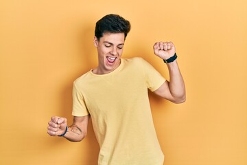 Young hispanic man wearing casual yellow t shirt dancing happy and cheerful, smiling moving casual and confident listening to music