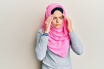 Young caucasian woman wearing traditional islamic hijab scarf with hand on head for pain in head because stress. suffering migraine.