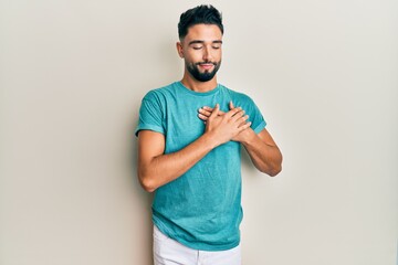 Young man with beard wearing casual clothes smiling with hands on chest, eyes closed with grateful gesture on face. health concept.