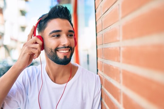 Young arab man smiling happy using headphones leaning on the wall at the city.