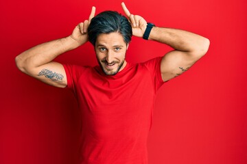 Fototapeta premium Young hispanic man wearing casual red t shirt posing funny and crazy with fingers on head as bunny ears, smiling cheerful