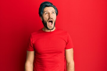 Young hispanic man wearing casual red t shirt angry and mad screaming frustrated and furious, shouting with anger. rage and aggressive concept.