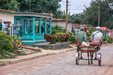 Escena en una calle del pueblo cubano de Viñales con hombres sobre un carro de caballos circulando entre las casas de madera 