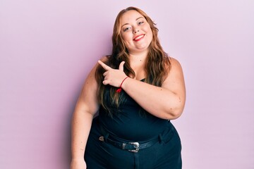 Plus size caucasian young woman wearing casual clothes over pink background smiling cheerful pointing with hand and finger up to the side