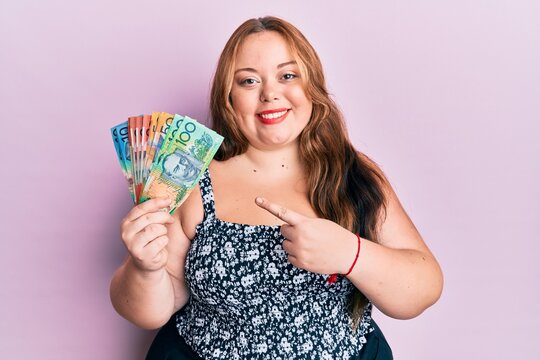 Plus size caucasian young woman holding australian dollars smiling happy pointing with hand and finger