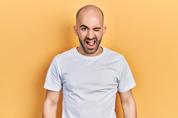 Young bald man wearing casual white t shirt winking looking at the camera with sexy expression,...