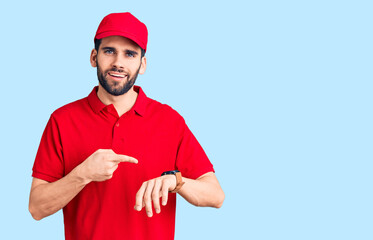 Young handsome man with beard wearing delivery uniform in hurry pointing to watch time, impatience,...