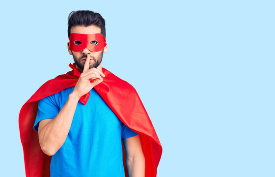Young handsome man with beard wearing super hero costume asking to be quiet with finger on lips. silence and secret concept.