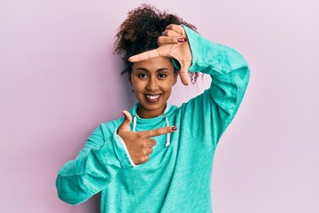 Beautiful african american woman with afro hair wearing casual sweatshirt smiling making frame with hands and fingers with happy face. creativity and photography concept.