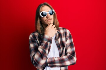 Handsome caucasian man with long hair wearing hipster shirt wearing sunglasses thinking concentrated about doubt with finger on chin and looking up wondering