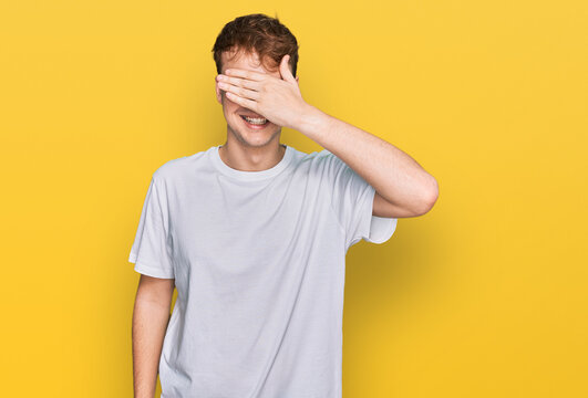 Young caucasian man wearing casual white t shirt smiling and laughing with hand on face covering eyes for surprise. blind concept.