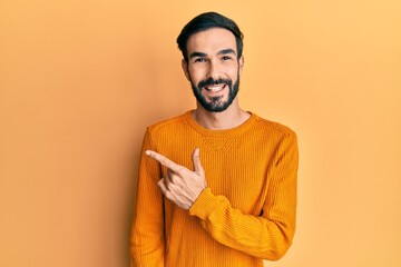 Young hispanic man wearing casual clothes cheerful with a smile of face pointing with hand and finger up to the side with happy and natural expression on face