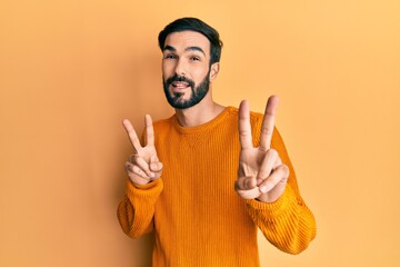 Fototapeta premium Young hispanic man wearing casual clothes smiling looking to the camera showing fingers doing victory sign. number two.