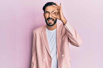 Young hispanic man wearing business jacket doing ok gesture with hand smiling, eye looking through fingers with happy face.