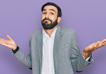Young hispanic man wearing business clothes clueless and confused expression with arms and hands...