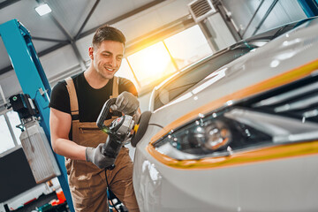 Auto mechanic worker polishing car at automobile repair and renew service station shop by power...