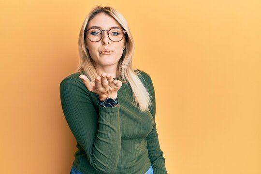 Young caucasian woman wearing casual clothes and glasses looking at the camera blowing a kiss with hand on air being lovely and sexy. love expression.