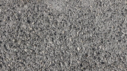 gray background of a cement structure with a small stone in a frozen surface, a fragment of an asphalt cloth close-up with interspersed small stones, a textured background of a ground road surface