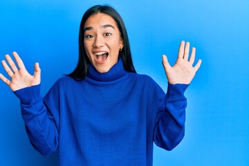 Young asian woman wearing casual winter sweater showing and pointing up with fingers number ten while smiling confident and happy.