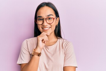 Young asian woman wearing casual clothes and glasses smiling looking confident at the camera with crossed arms and hand on chin. thinking positive.